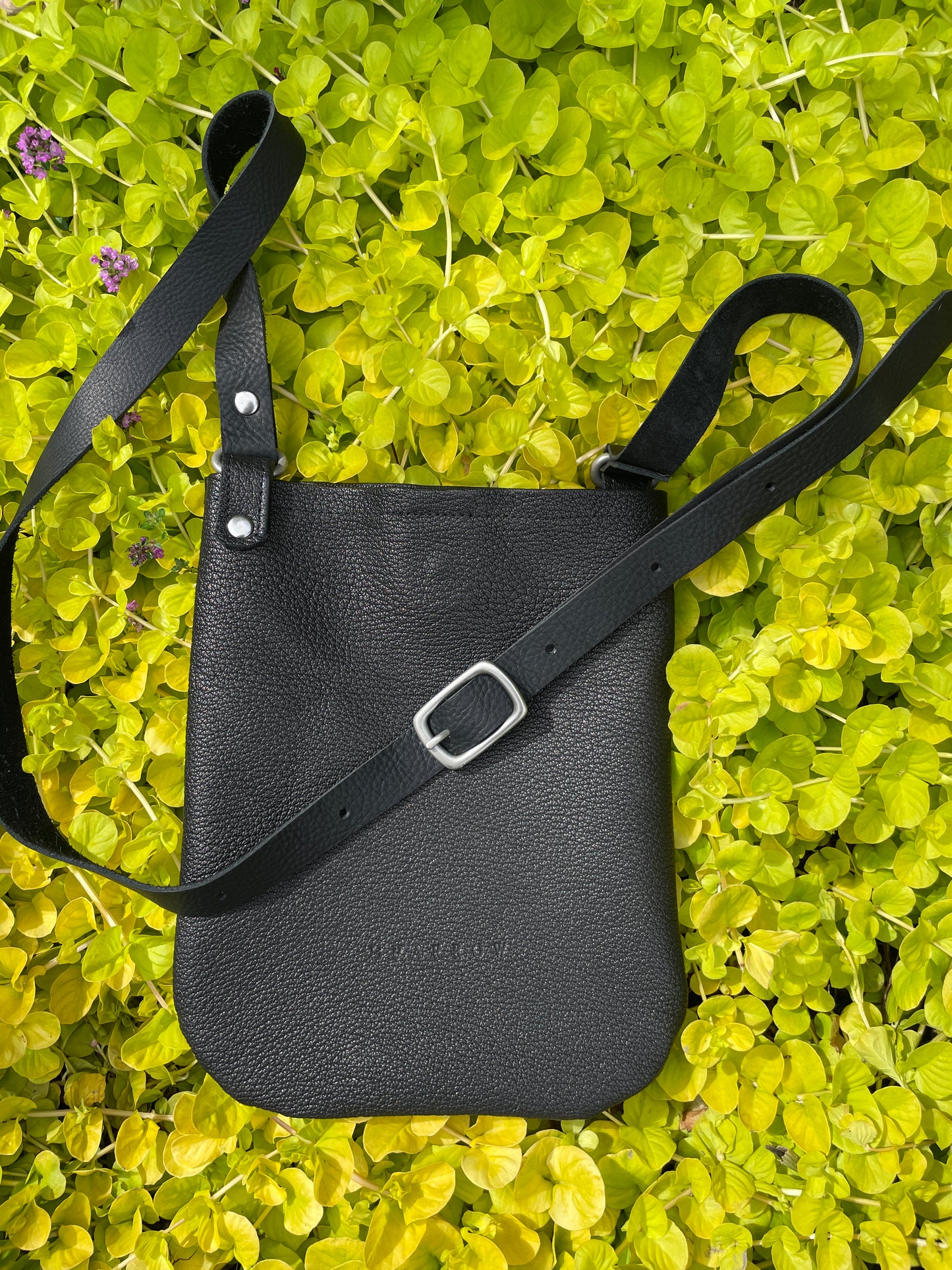 Black leather bag with a strap on a green leafy background