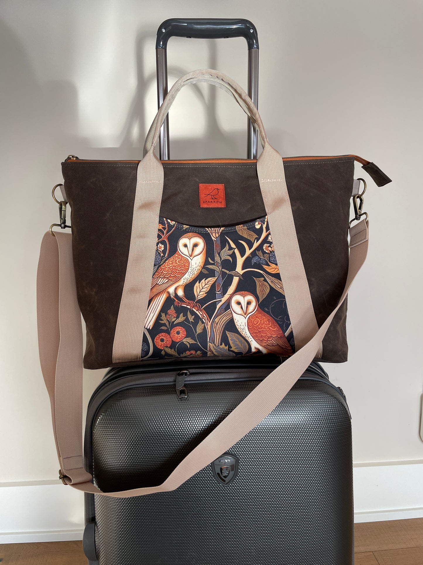 Oxbow crossbody/tote bag in waxed canvas exterior, with tan nylon adjustable strap and handles. Two exterior front pockets, multiple inner pocket, fully lined. chocolate brown waxed canvas, owl print on accent front and back pockets.