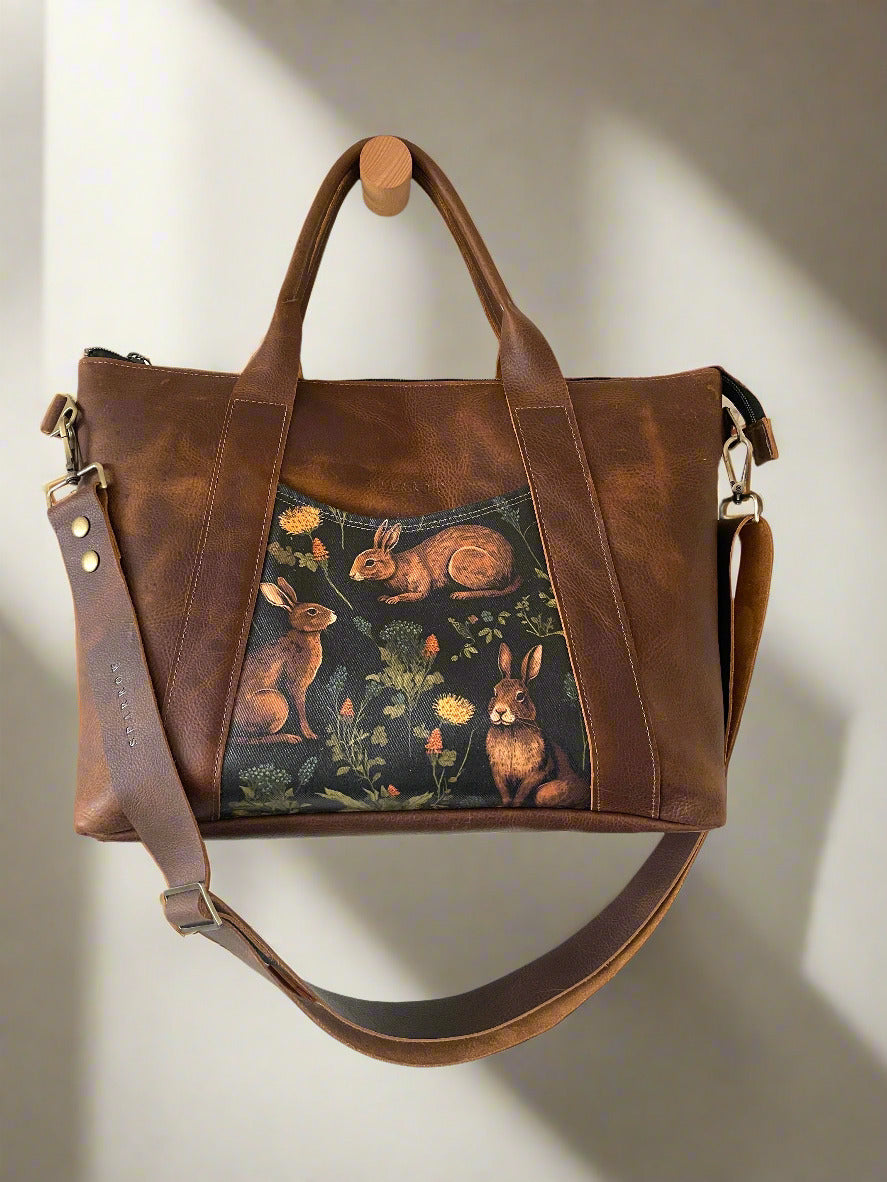 Handcrafted tote/crossbody bag in brown full-grain leather and rabbit print pocket accents.