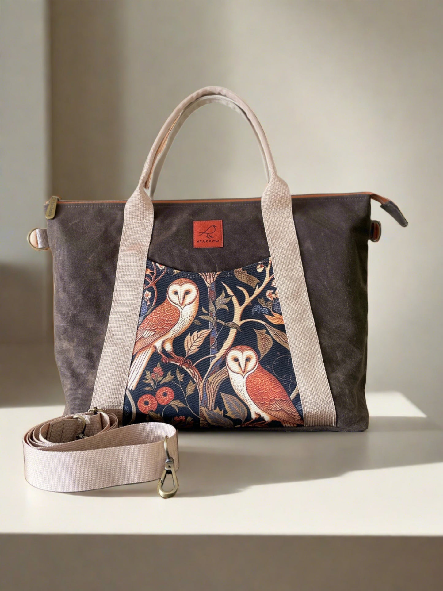 Spacious vegan tote bag with adjustable and removable crossbody strap. 2 outer slip pockets, fully lined interior with divided slip pockets and a zippered pocket, a key ring. Strap on the back to attach securely to the pull-up handle on luggage. Front pattern: 2 owls. Cream nylon straps, brown waxed canvas body, tan waterproof canvas lining.
