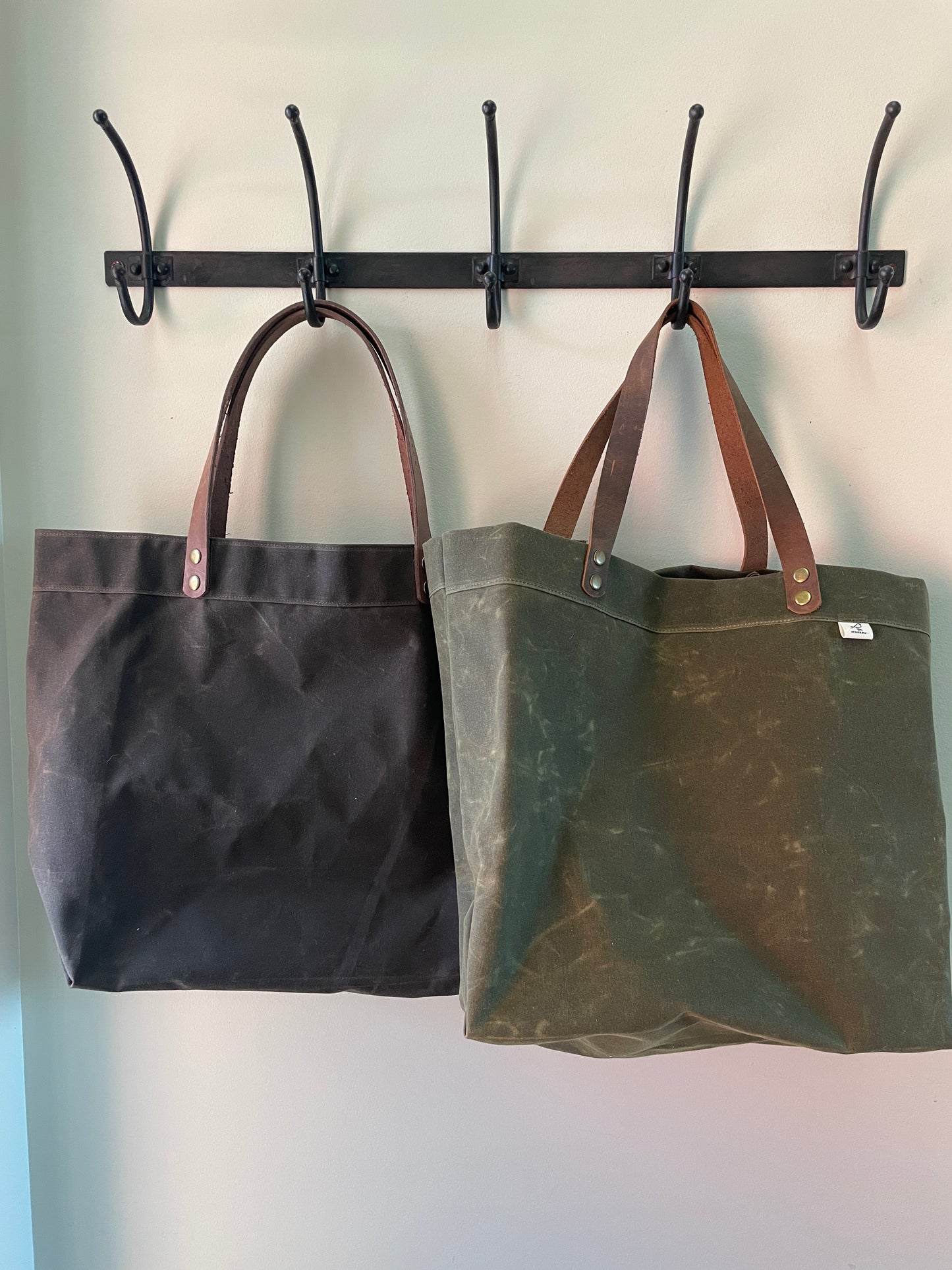 Handmade simple waxed canvas shopping tote with full-grain leather handles, available in olive green or chocolate brown.