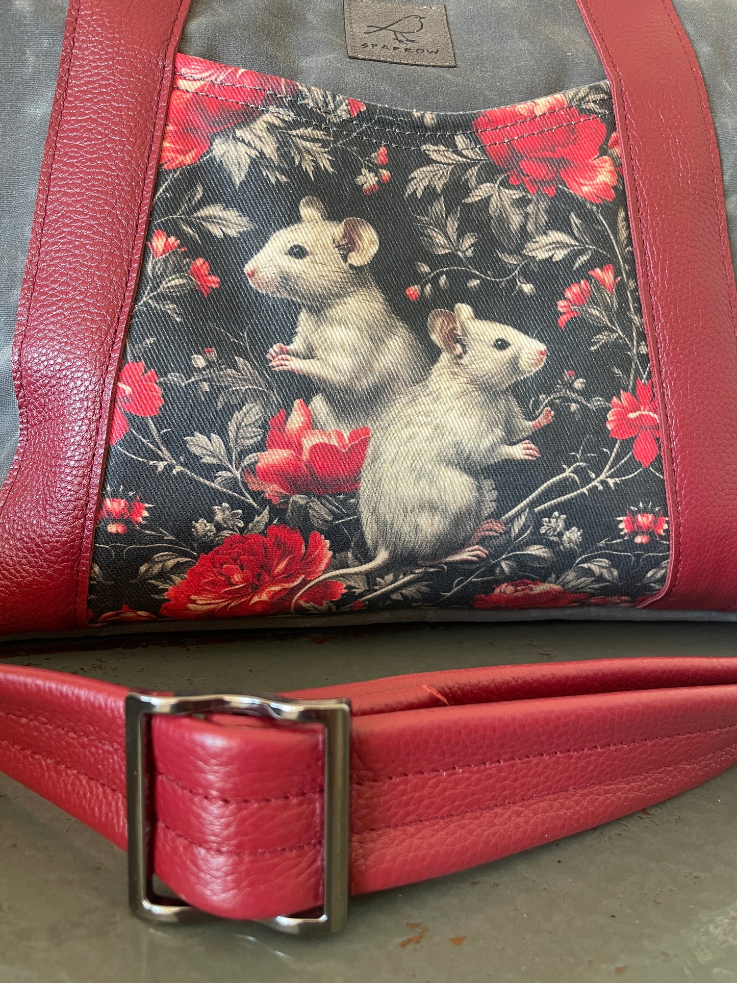 Oxbow crossbody/tote bag in waxed canvas exterior, with leather adjustable strap and handles. Two exterior front pockets, multiple inner pocket, fully lined. Grey waxed canvas, mice print on accent front and back pockets. red leather.