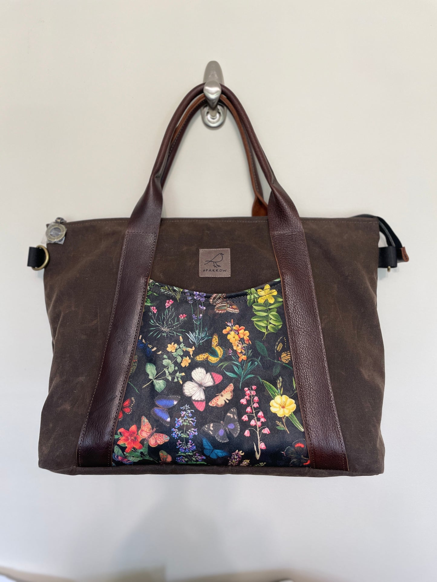 Oxbow crossbody/tote bag in waxed canvas exterior, with leather adjustable strap and handles. Two exterior front pockets, multiple inner pocket, fully lined. Chocolate brown waxed canvas, midnight garden print on accent front and back pockets.