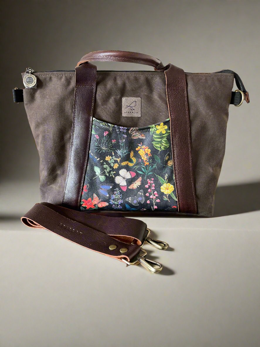 Oxbow crossbody/tote bag in waxed canvas exterior, with leather adjustable strap and handles. Two exterior front pockets, multiple inner pocket, fully lined. chocolate brown waxed canvas, midnight garden floral print on accent front and back pockets.