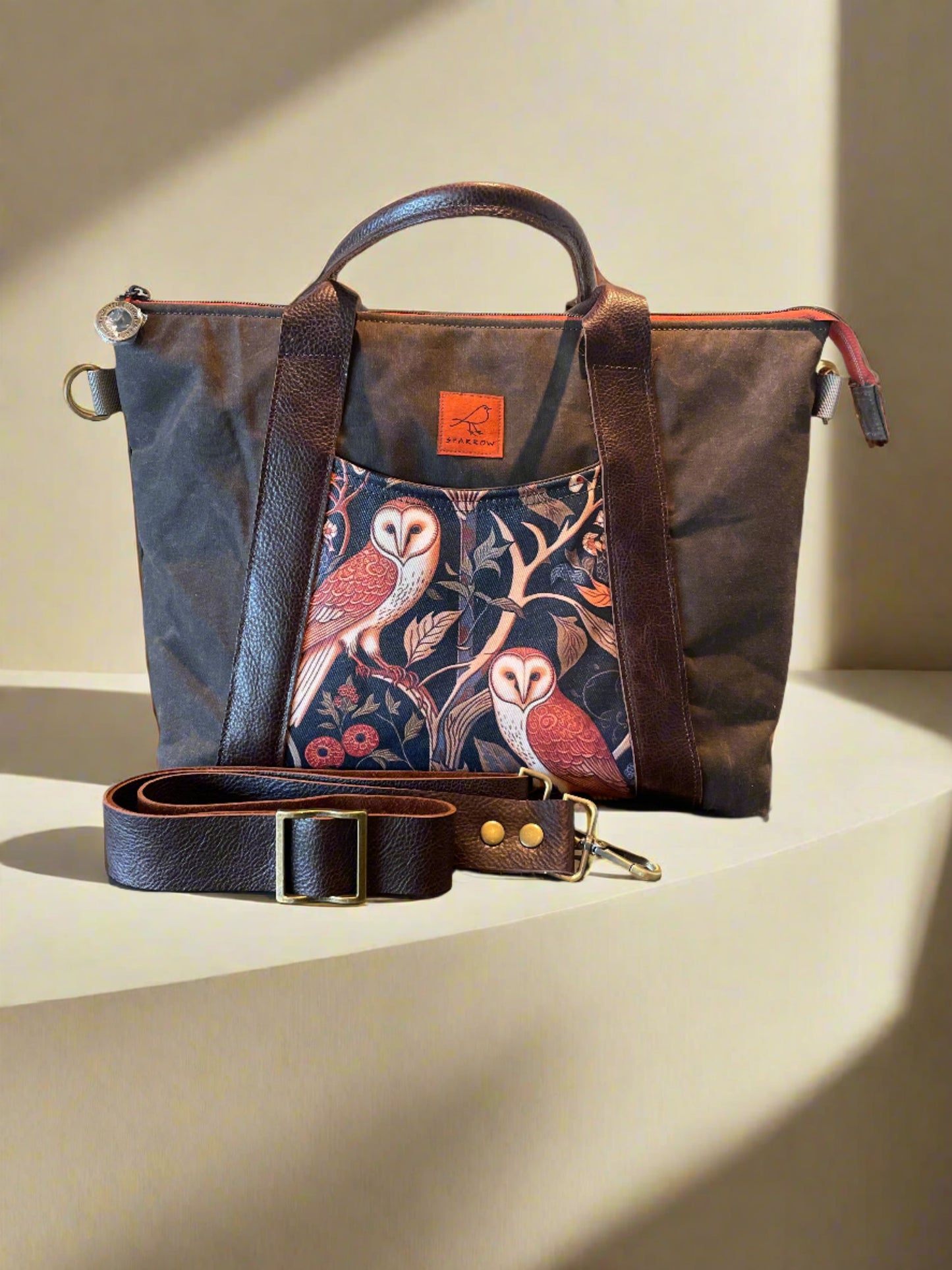 Oxbow crossbody/tote bag in waxed canvas exterior, with leather adjustable strap and handles. Two exterior front pockets, multiple inner pocket, fully lined. chocolate brown waxed canvas, owl print on accent front and back pockets.