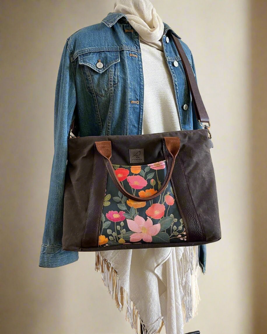 Oxbow crossbody/tote bag in waxed canvas exterior, with leather adjustable strap and handles. Two exterior front pockets, multiple inner pocket, fully lined. chocolate brown waxed canvas, floral print on accent front and back pockets.