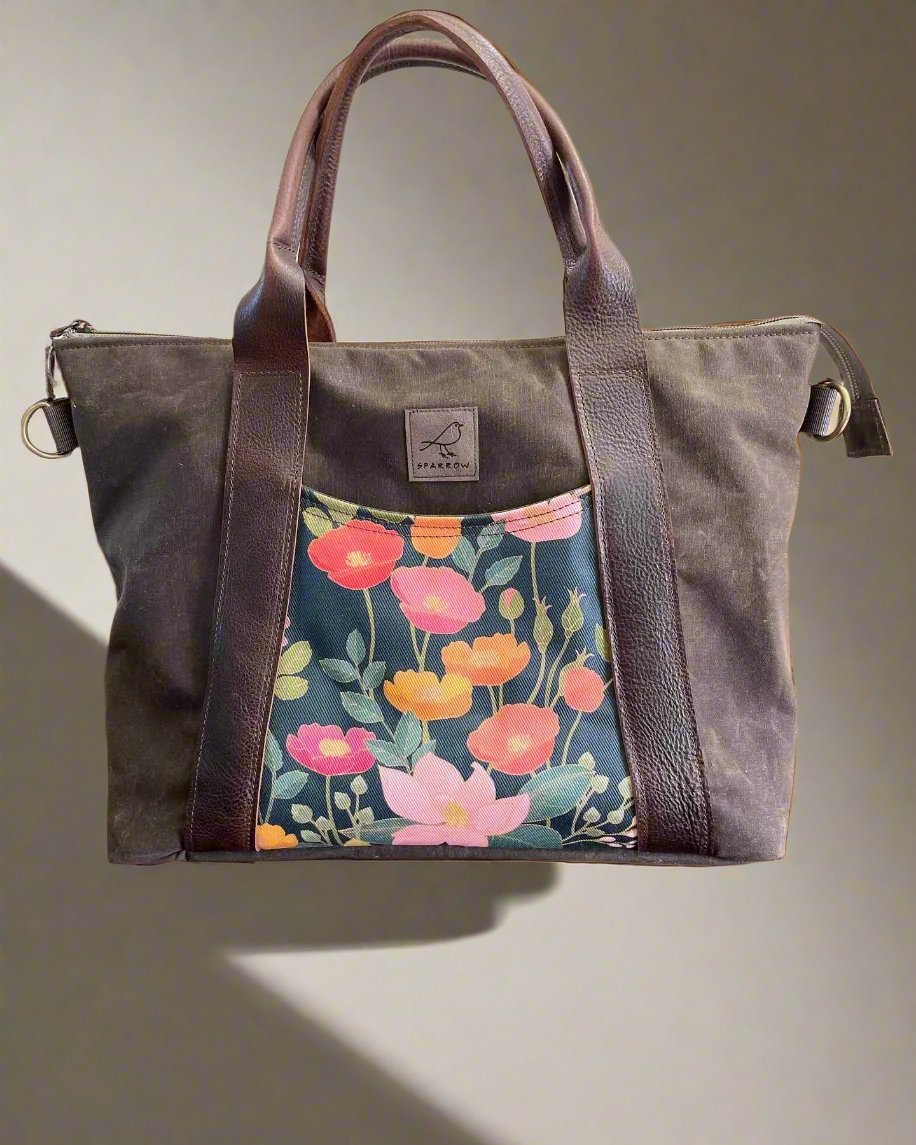 Oxbow crossbody/tote bag in waxed canvas exterior, with leather adjustable strap and handles. Two exterior front pockets, multiple inner pocket, fully lined. Chocolate brown waxed canvas, floral print on accent front and back pockets.