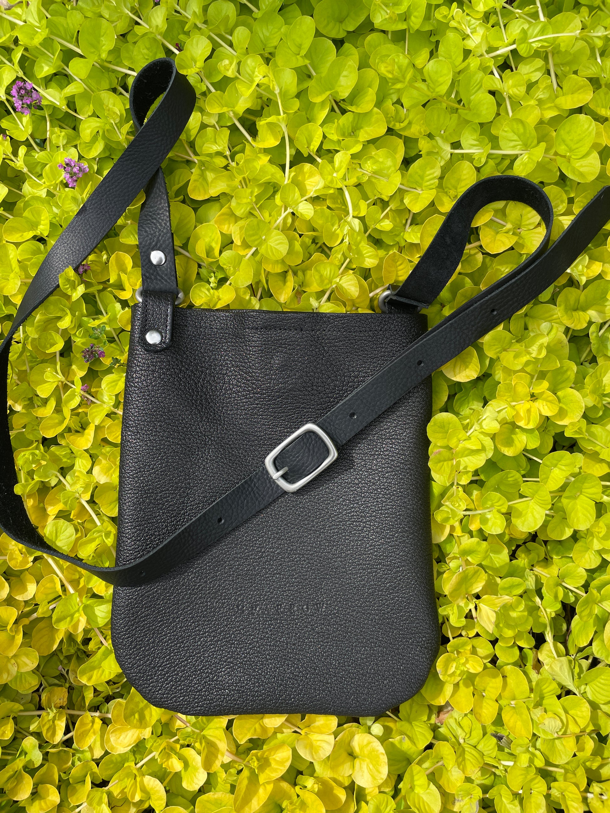 Black leather bag with a strap on a green leafy background