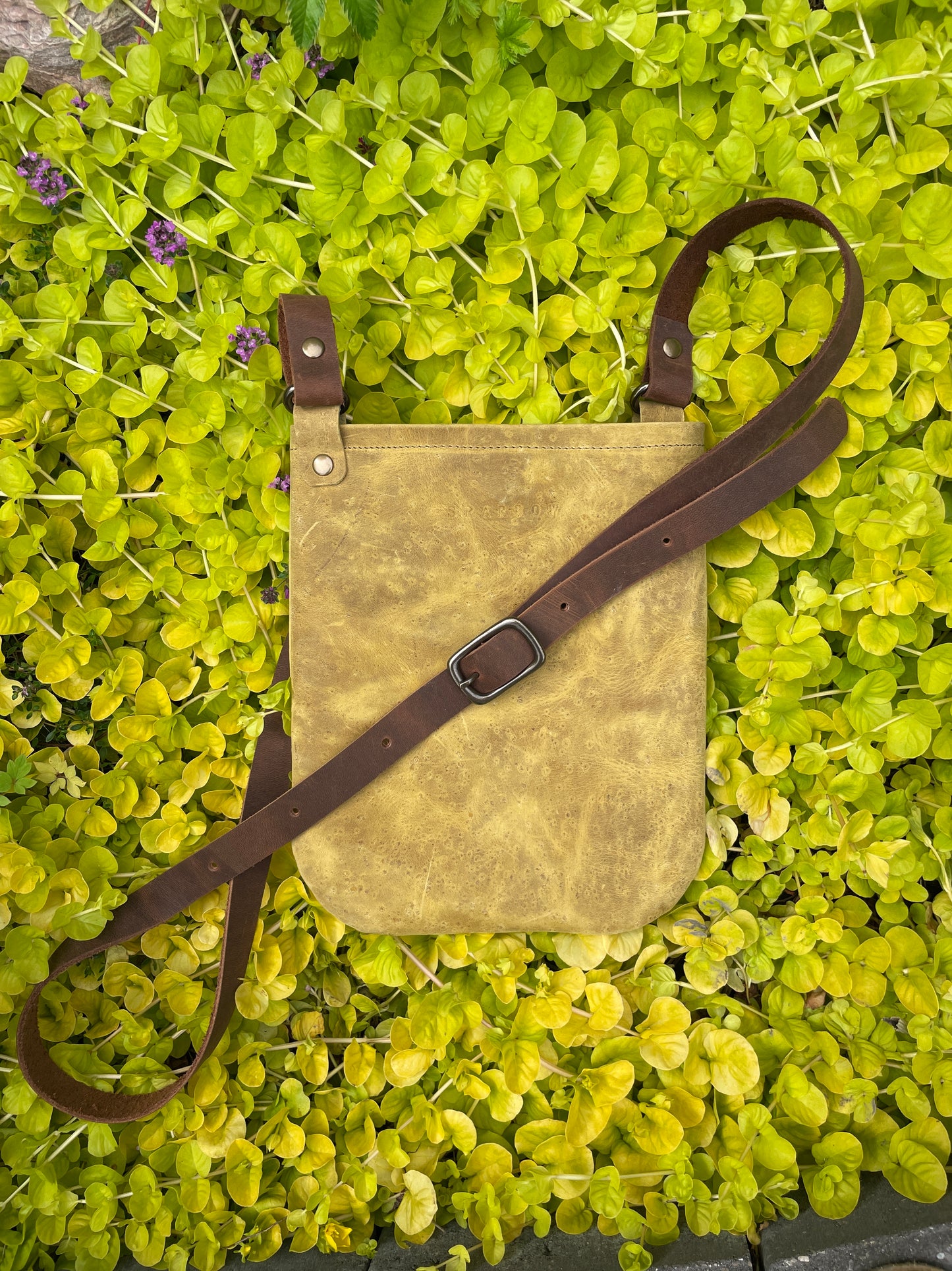 Laredo Sunset yellow Waxed canvas bag with a brown strap on a green leafy background