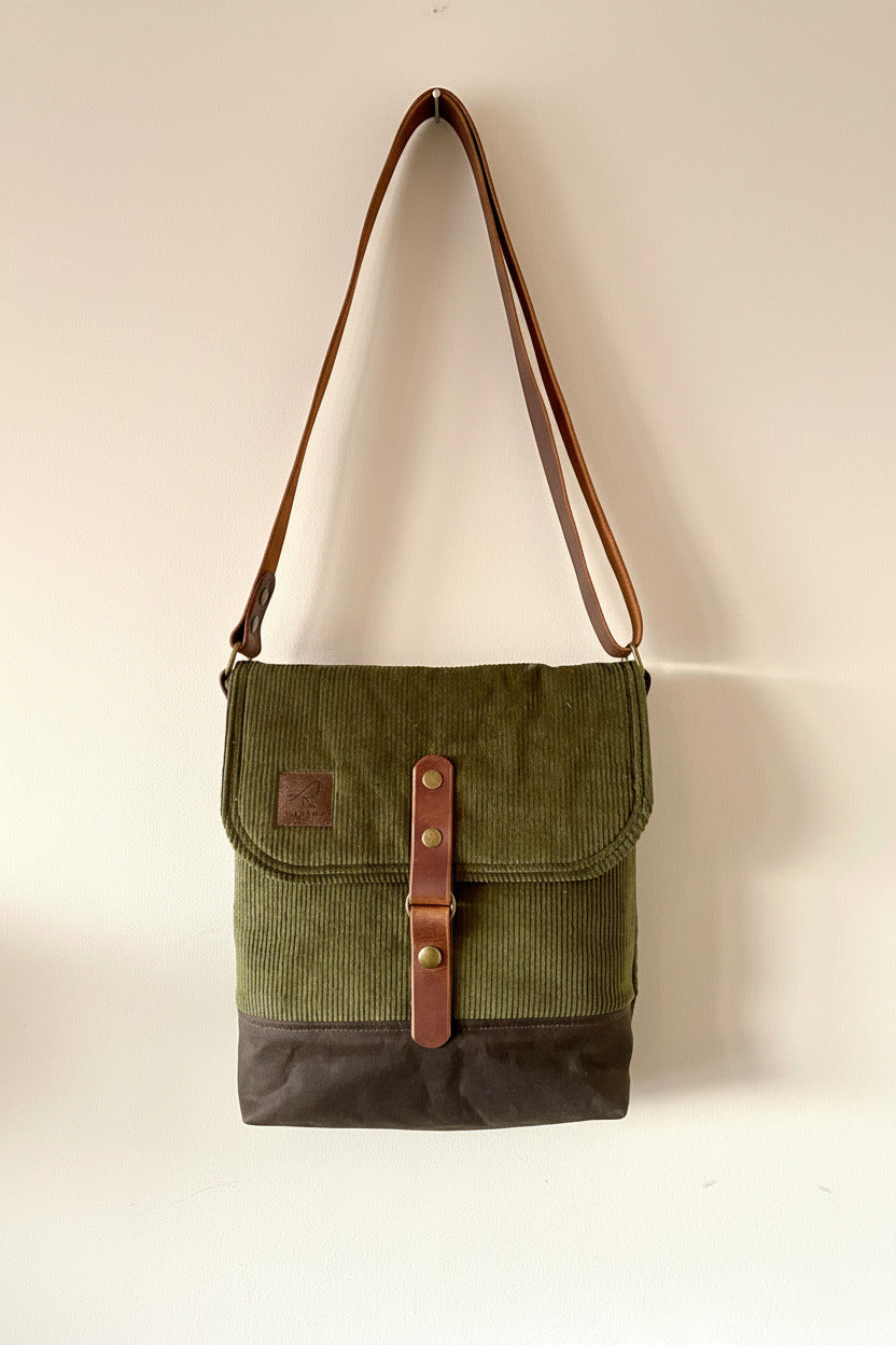 Messenger crossbody bag in olive green corduroy on main body and top flap, with chocolate brown waxed canvas base and 1.5" adjustable leather cross-body strap and 1" wide leather front closure. Handcrafted by Sparrow Handmade in Canada. 