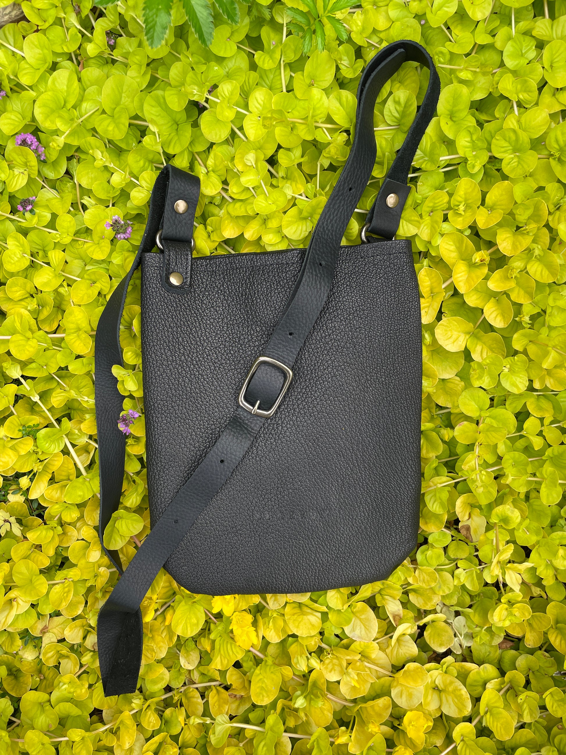 Black leather bag with a strap on green leafy background