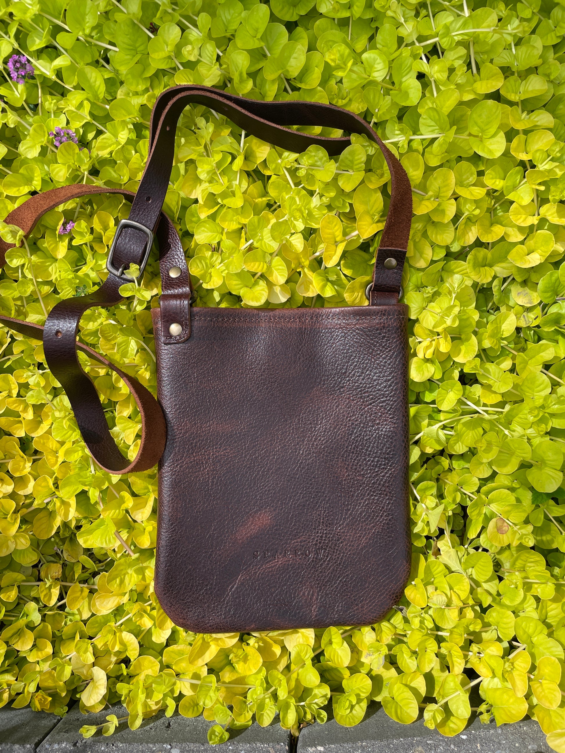 Brown leather crossbody bag on a green leafy background