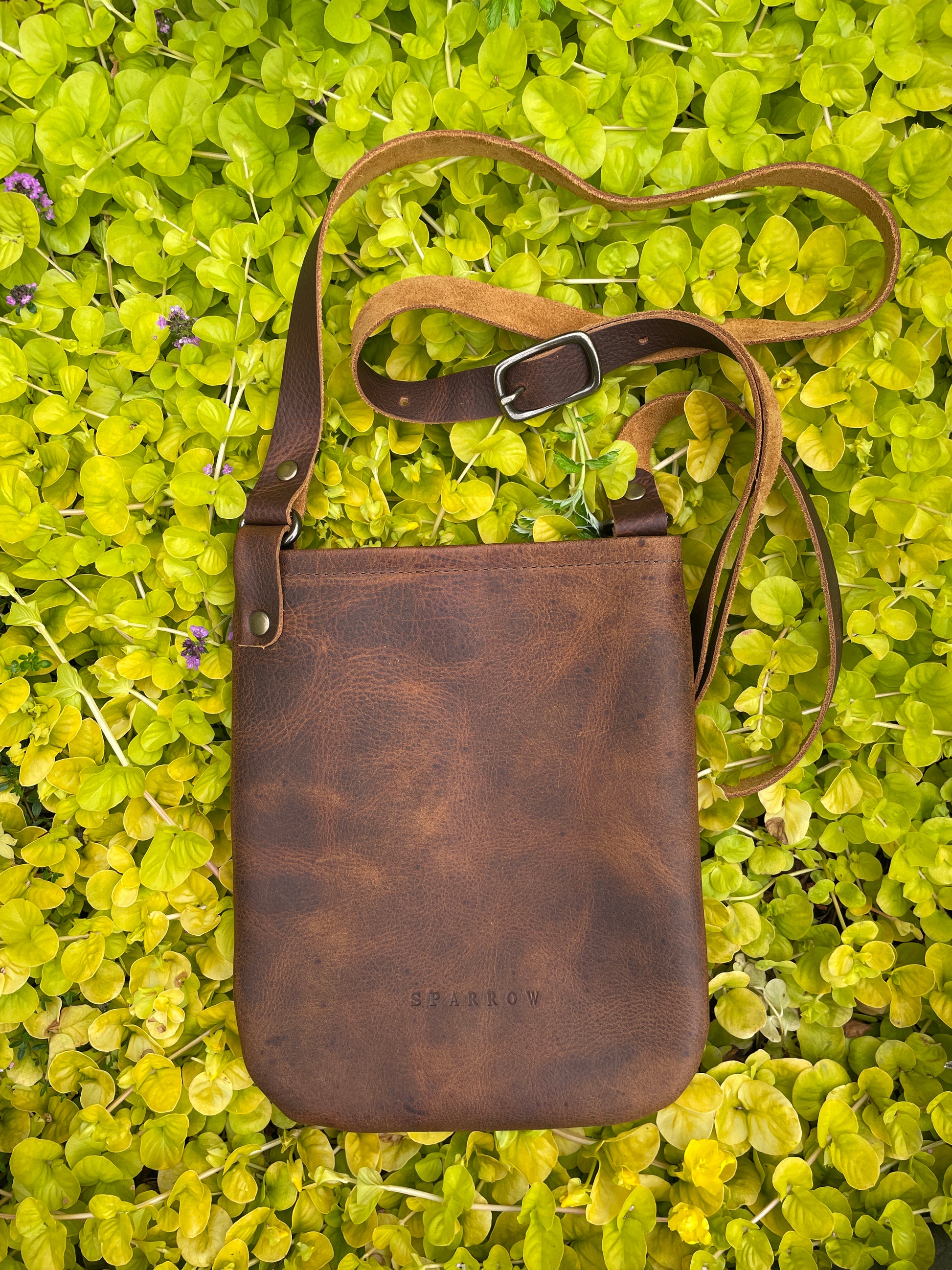 Brown leather crossbody bag on a green leafy background