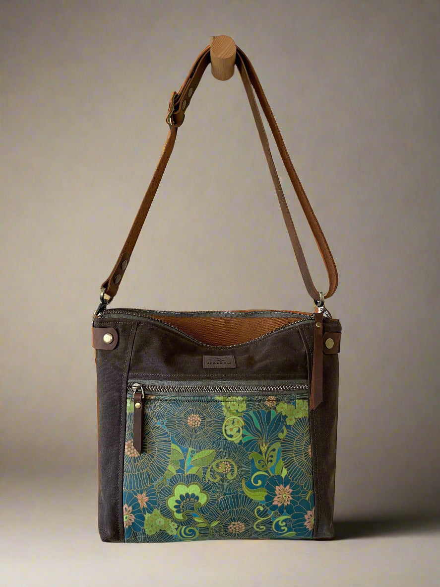 Ready-to-ship Cambridge crossbody/shoulder bag in chocolate waxed canvas, retro floral accent, cinnamon denim lining, and full-grain leather adjustable strap and accents. Handcrafted in Calgary, Canada. waxed canvas bag. 