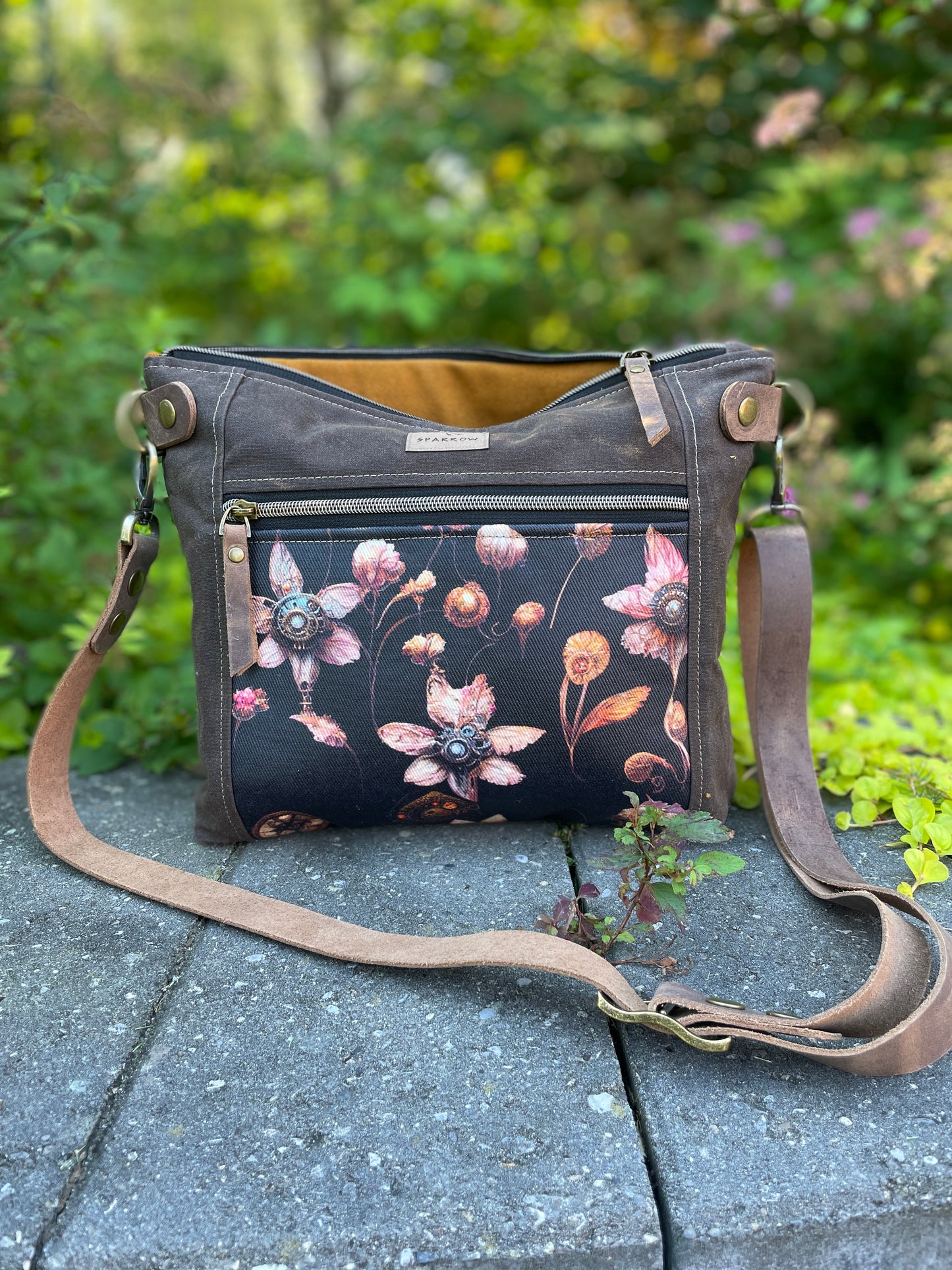 Cambridge crossbody bag in brown waxed canvas and steampunk floral front pocket accent print, with zippered front pocket and top closure. Cinnamon lining. Adjustable leather strap. Handcrafted in Canada by Sparrow Handmade.