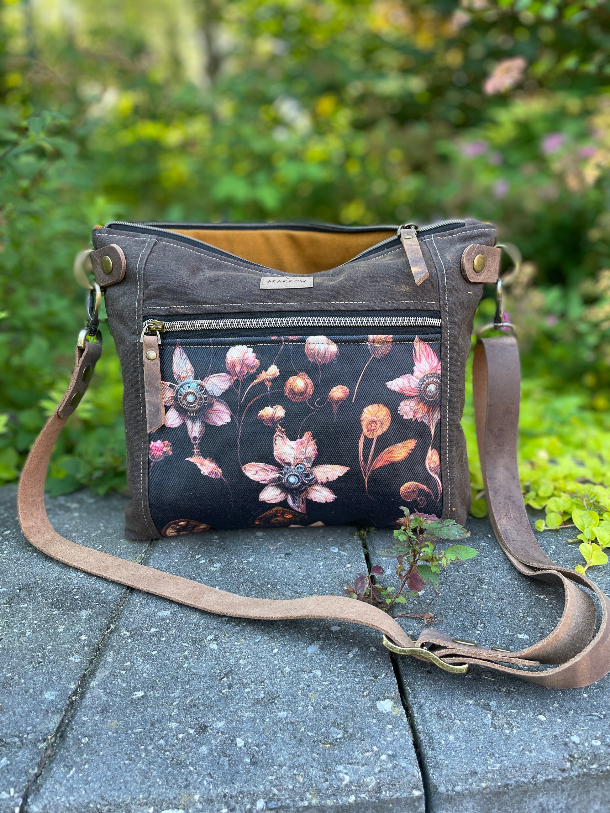 Cambridge crossbody bag in brown waxed canvas and steampunk floral front pocket accent print, with zippered front pocket and top closure. Cinnamon lining. Adjustable leather strap. Handcrafted in Canada by Sparrow Handmade.