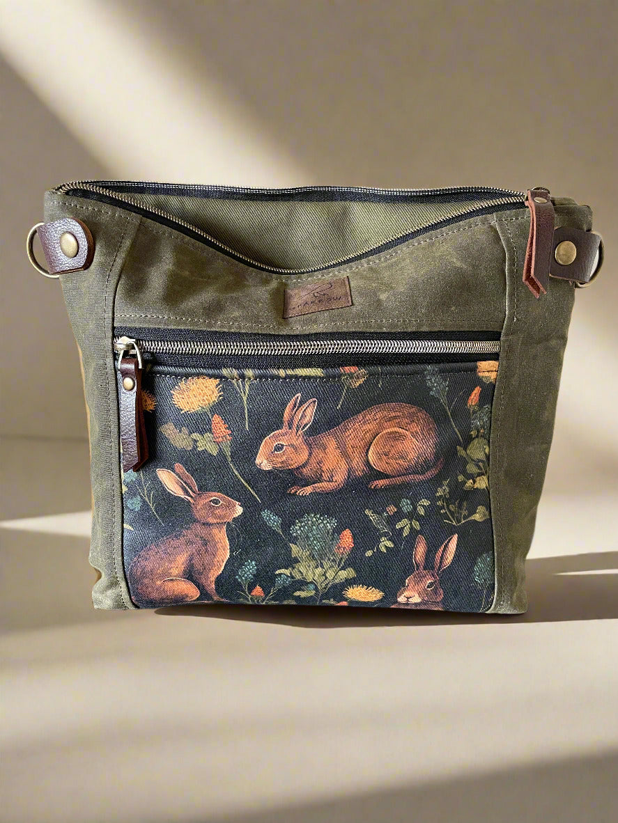 Cambridge crossbody bag in olive waxed canvas and medieval rabbitsl front pocket accent print, with zippered front pocket and top closure. Olive green lining. Adjustable leather strap. Handcrafted in Canada by Sparrow Handmade.