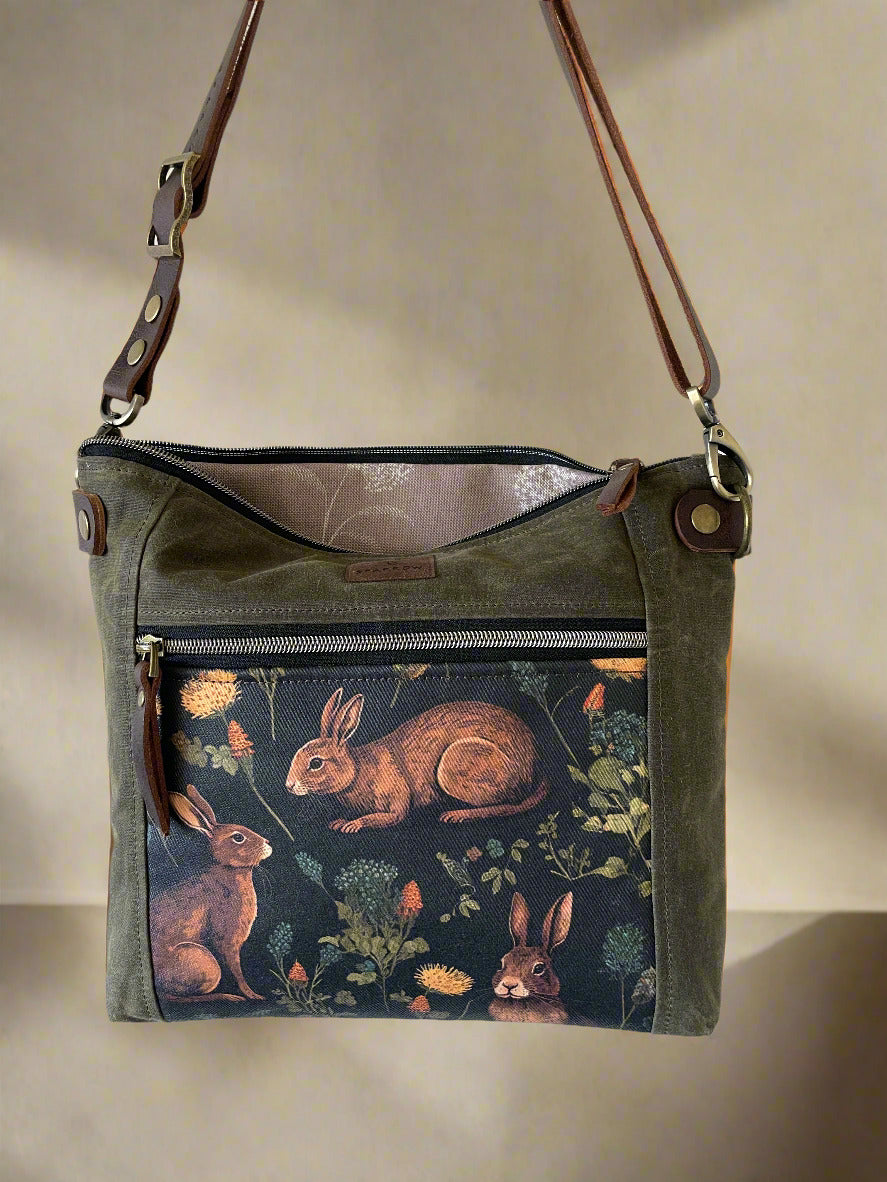 Cambridge crossbody bag in olive waxed canvas and medieval rabbitsl front pocket accent print, with zippered front pocket and top closure. Tan floral lining. Adjustable leather strap. Handcrafted in Canada by Sparrow Handmade.
