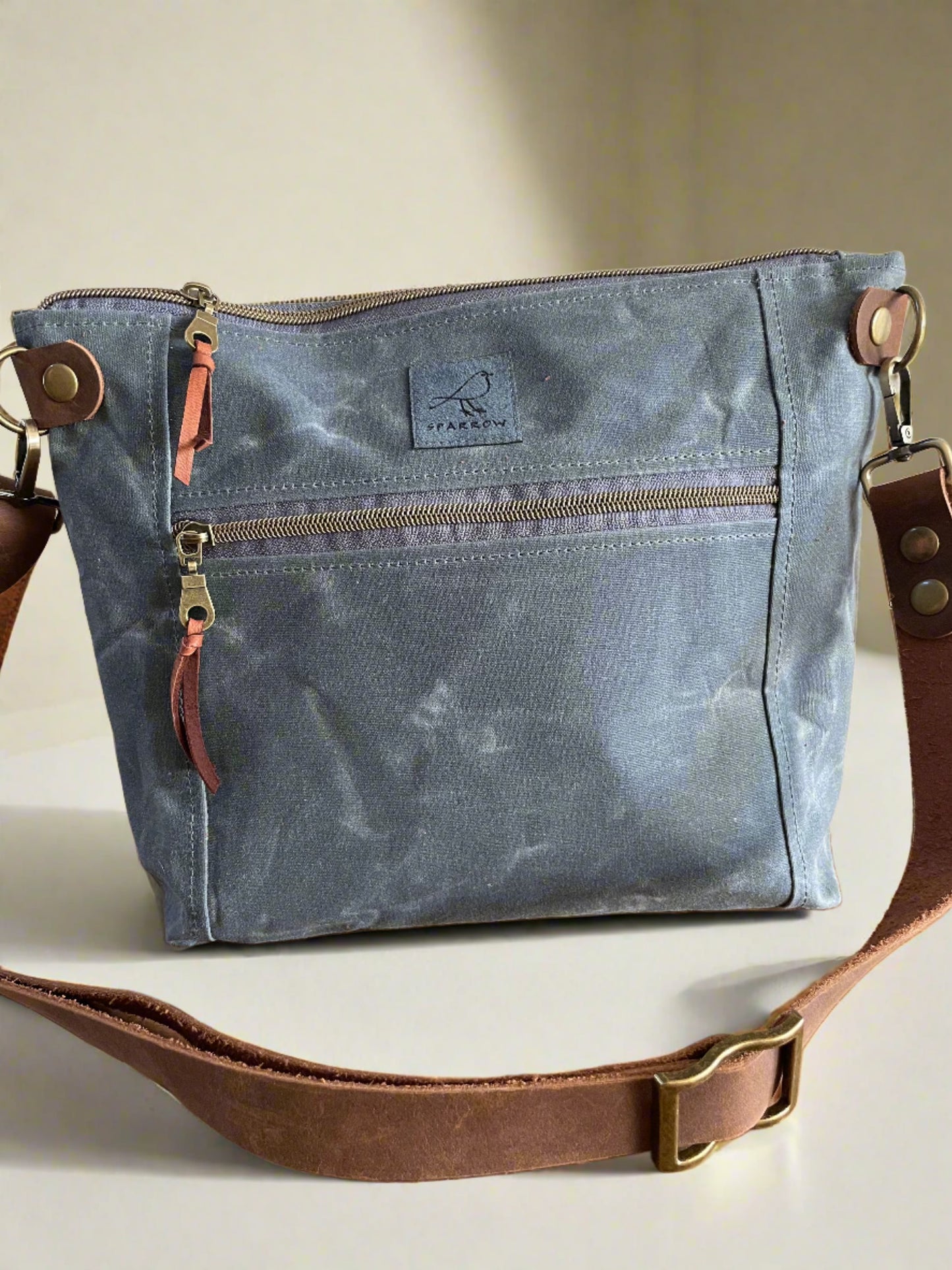 Cambridge crossbody bag in slate blue waxed canvas, with zippered front pocket and top closure. Adjustable leather strap. Handcrafted in Canada by Sparrow Handmade.