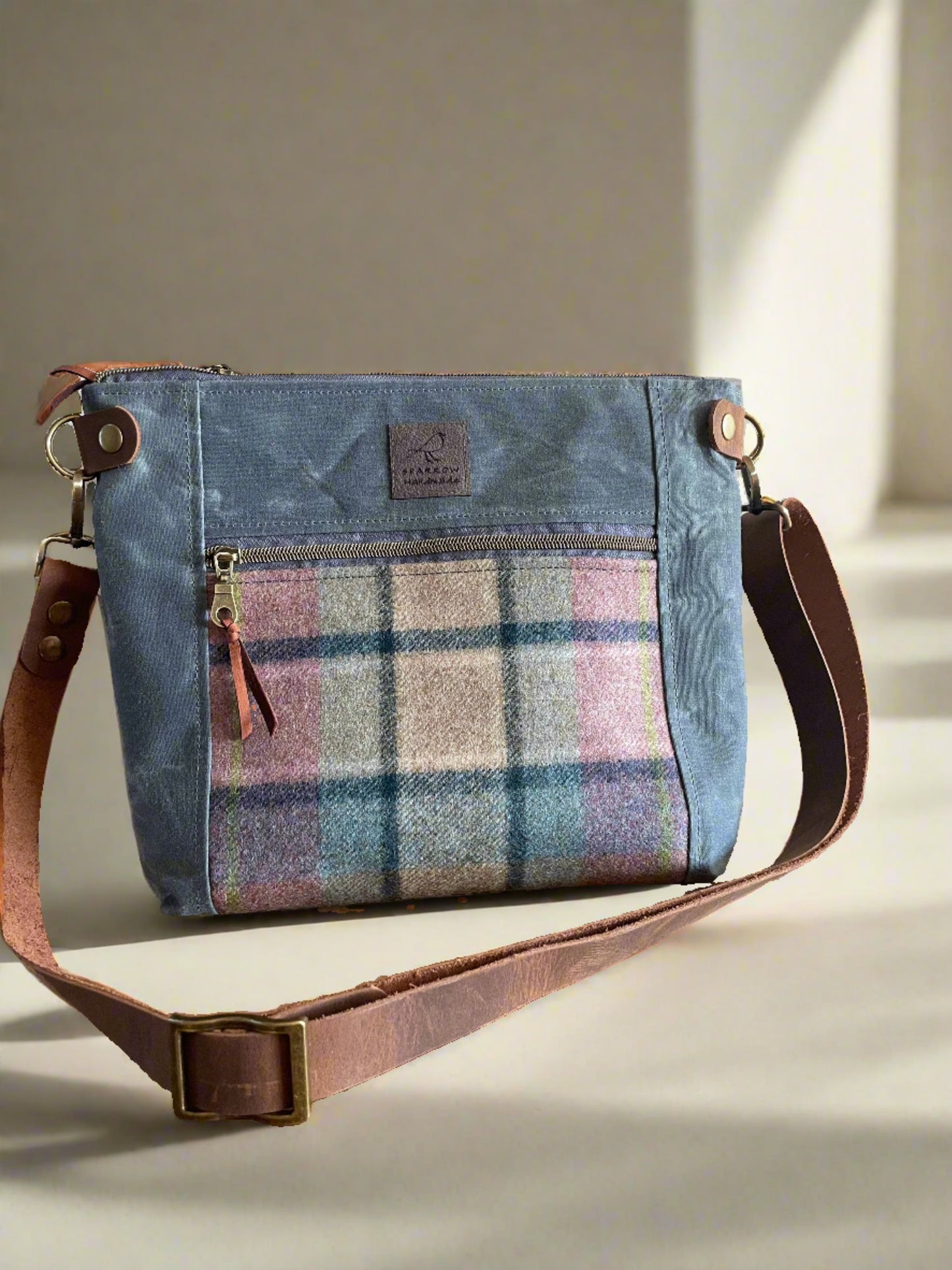 Cambridge crossbody bag in slate blue waxed canvas and pink, tan and blue wool plaid front pocket accent print, with zippered front pocket and top closure. Adjustable leather strap. Handcrafted in Canada by Sparrow Handmade.