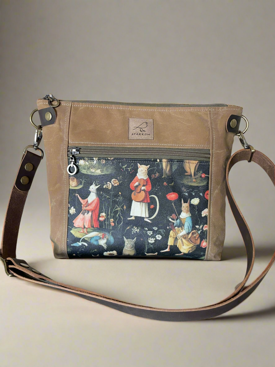 Cambridge crossbody bag in field tan waxed canvas and Hieronymous Bosch cats front pocket accent print, with zippered front pocket and top closure.  Adjustable leather strap. Handcrafted in Canada by Sparrow Handmade.