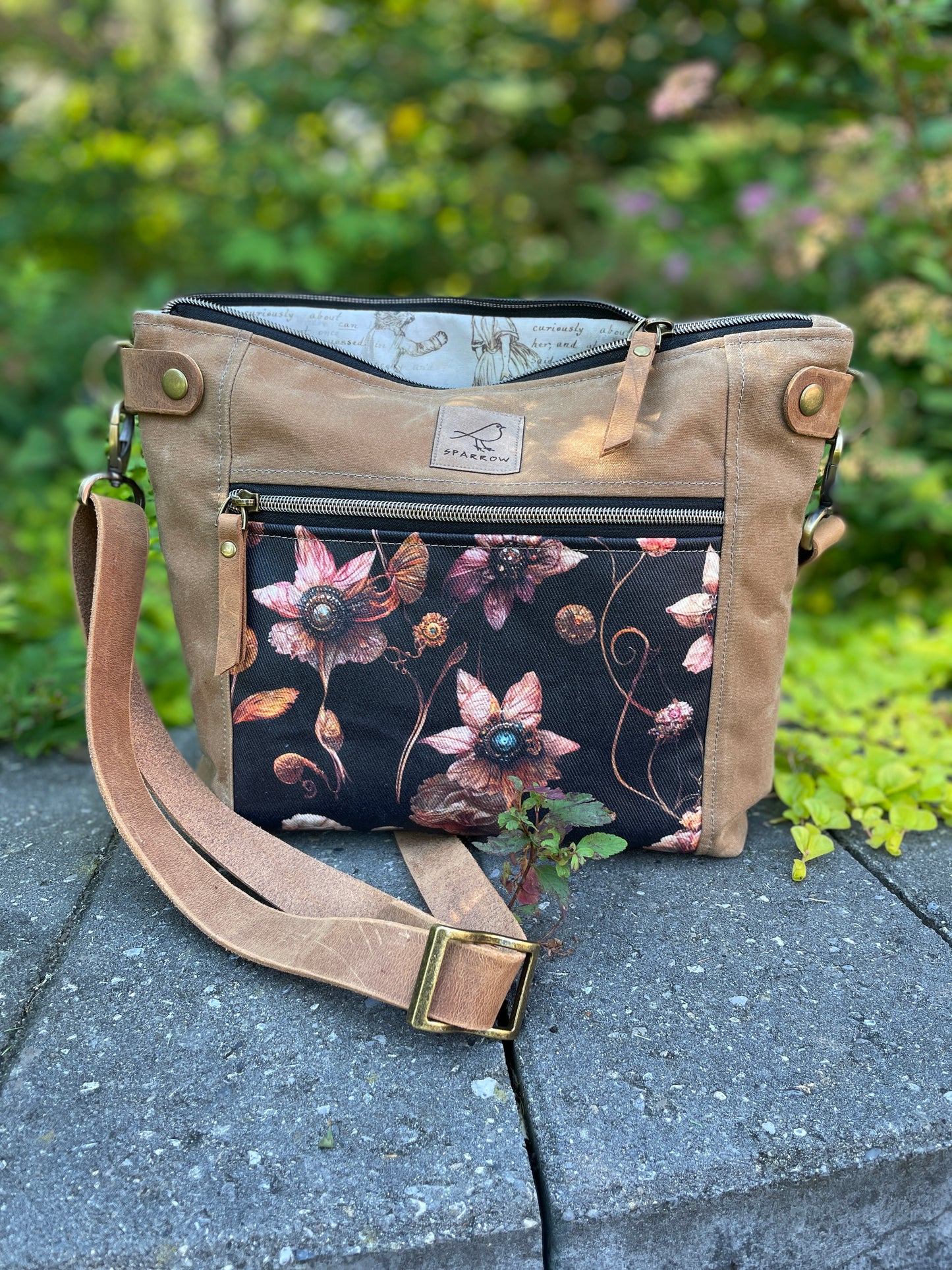 Cambridge crossbody bag in light tanwaxed canvas and steampunk floral front pocket accent print, with zippered front pocket and top closure. Alice in Wonderland lining. Adjustable leather strap. Handcrafted in Canada by Sparrow Handmade.