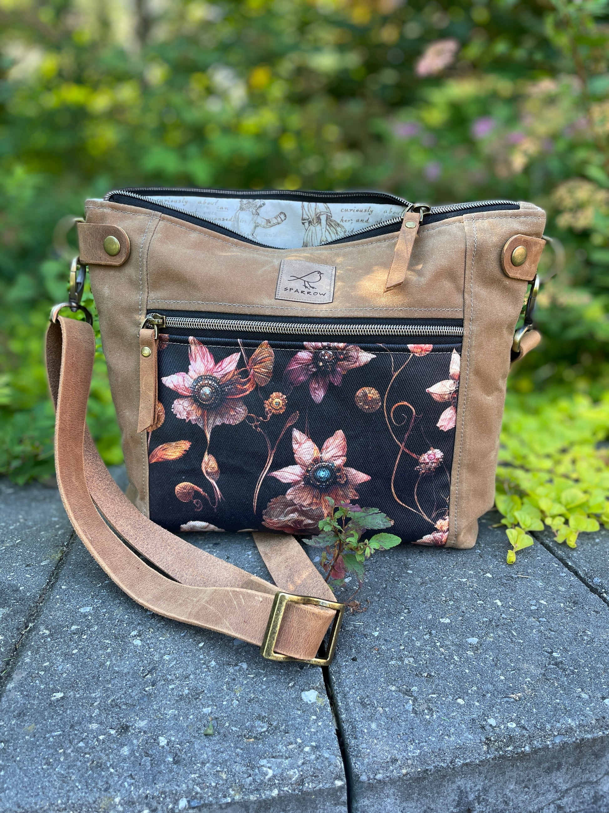 Cambridge crossbody bag in light tanwaxed canvas and steampunk floral front pocket accent print, with zippered front pocket and top closure. Alice in Wonderland lining. Adjustable leather strap. Handcrafted in Canada by Sparrow Handmade.