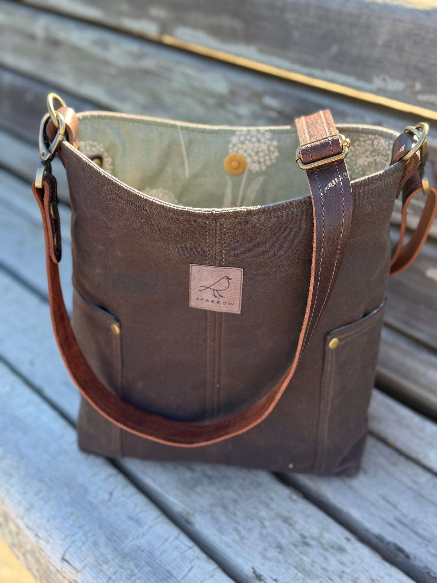 Compass crossbody bag on a bench in brown waxed canvas and green floral lining, handmade in Canada by Sparrow handmade. 
