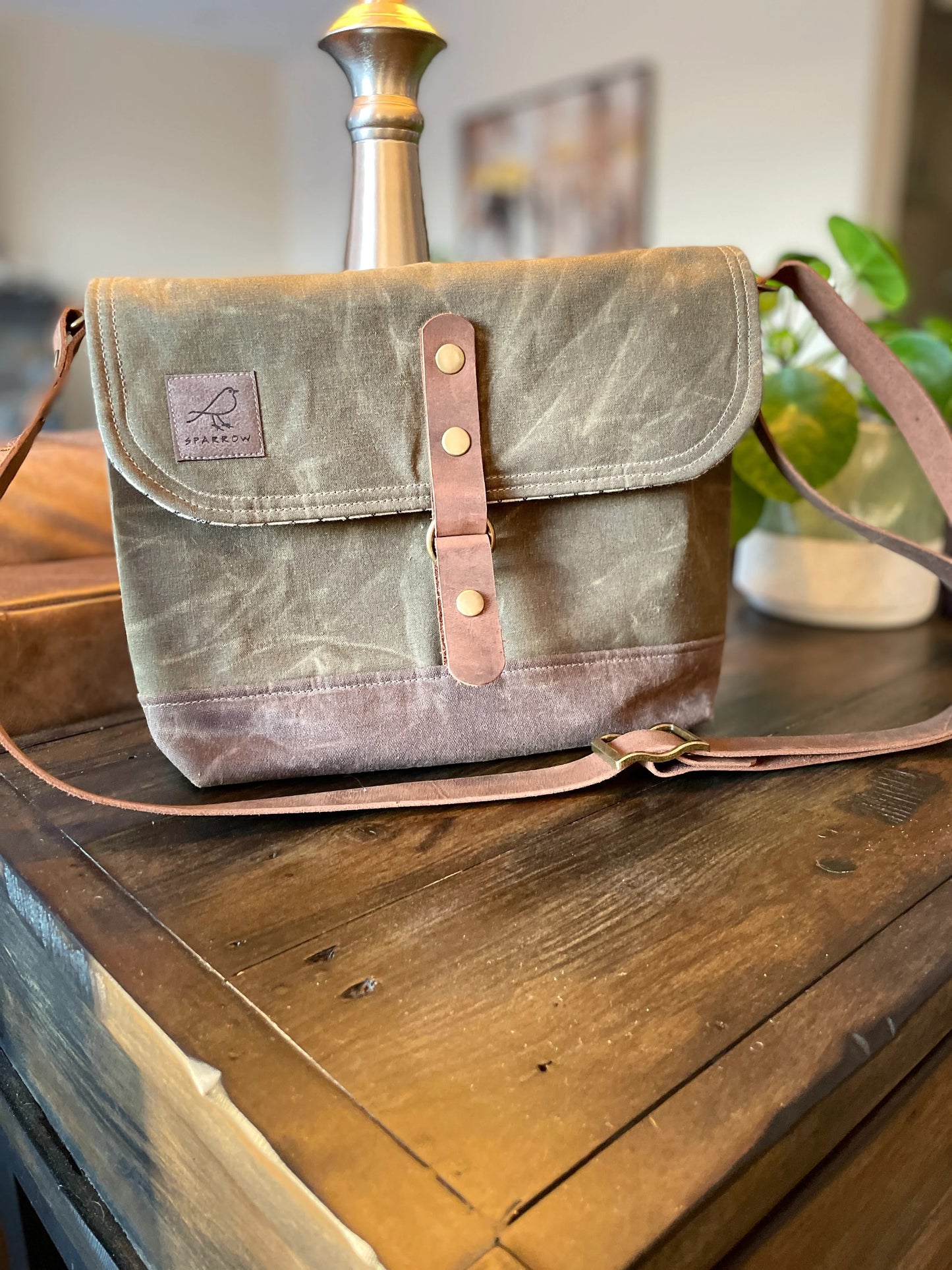 Shortie Messenger bag in olive green waxed canvas and a brown waxed canvas base. Brown leather 1.5 inch adjustable strap with a leather snap closure. Unisex bag. 