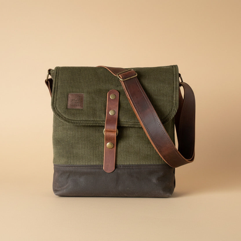 Messenger crossbody bag in olive green corduroy on main body and top flap, with chocolate brown waxed canvas base and 1.5" adjustable leather cross-body strap and 1" wide leather front closure. Handcrafted by Sparrow Handmade in Canada. 