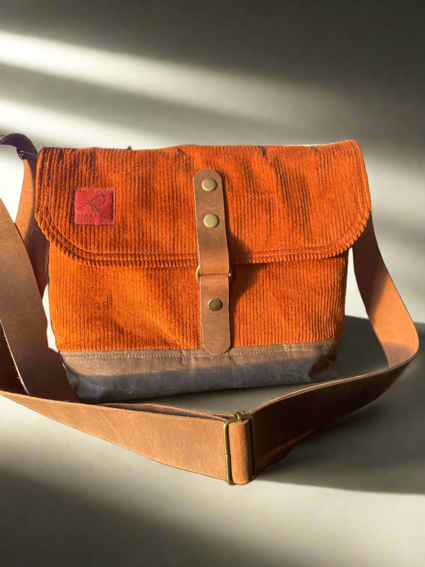 Shortie Messenger bag in burnt orange corduroy and a brown waxed canvas base. Brown leather 1.5 inch adjustable strap with a leather snap closure. Unisex bag. 