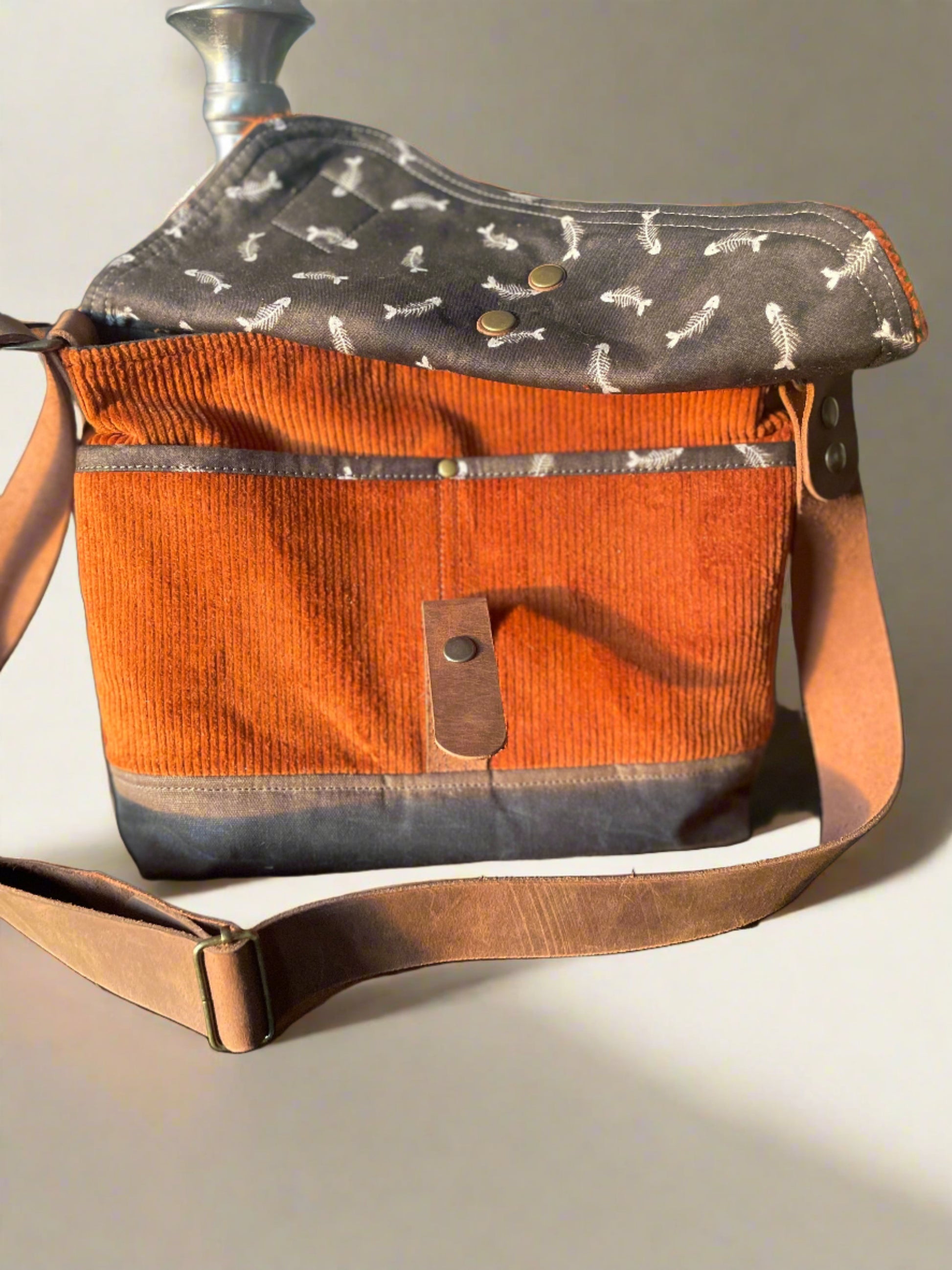 Shortie Messenger bag in burnt orange corduroy and a brown waxed canvas base. Brown leather 1.5 inch adjustable strap with a leather snap closure. Unisex bag. 