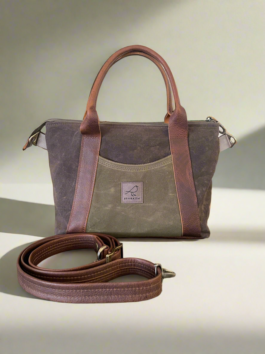 A brown waxed canvas mini Oxbow tote/crossbody bag with an olive green waxed canvas front and back pocket.  Leather adjustable strap and handles. 