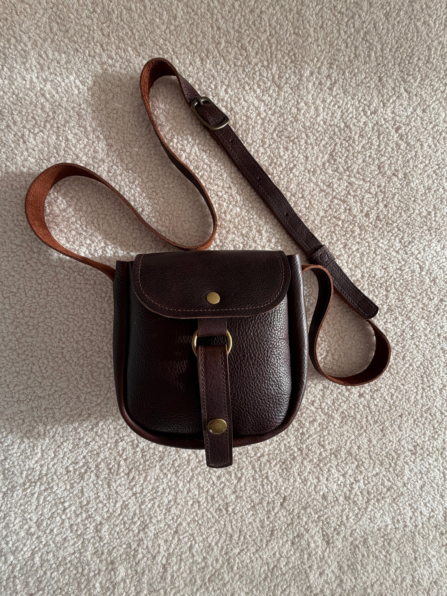 Brown leather bag with strap on a textured white surface