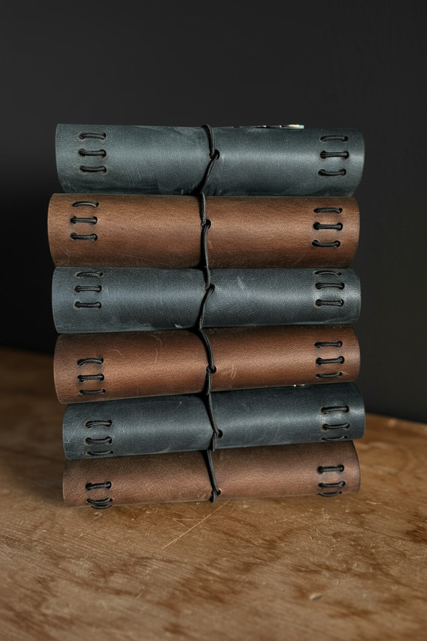 Stack of refillable leather traveler's journals with green metal feather embellishment on a desk, handcrafted in Calgary by Sparrow Handmade