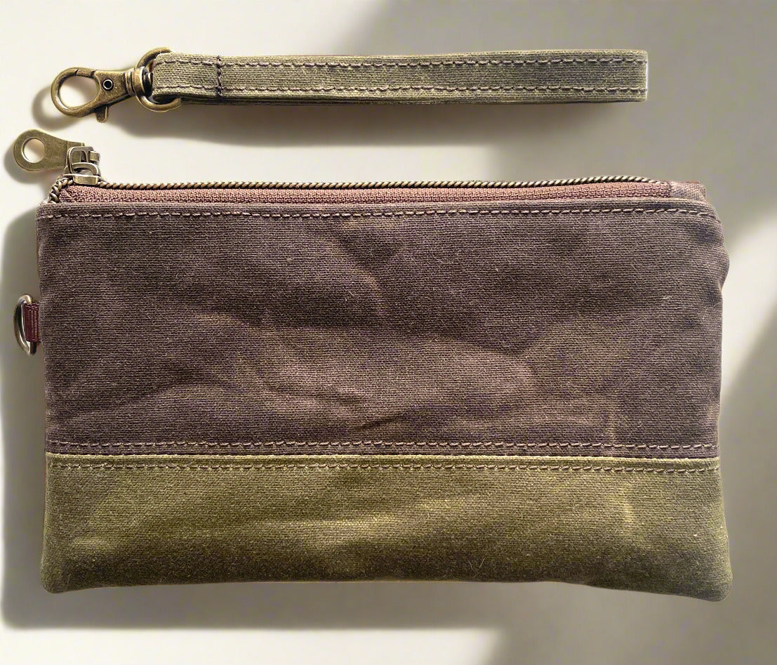 Two-tone zippered pouch. Top is brown waxed canvas, bottom third is olive green. Shows waxed canvas wrist strap also. 