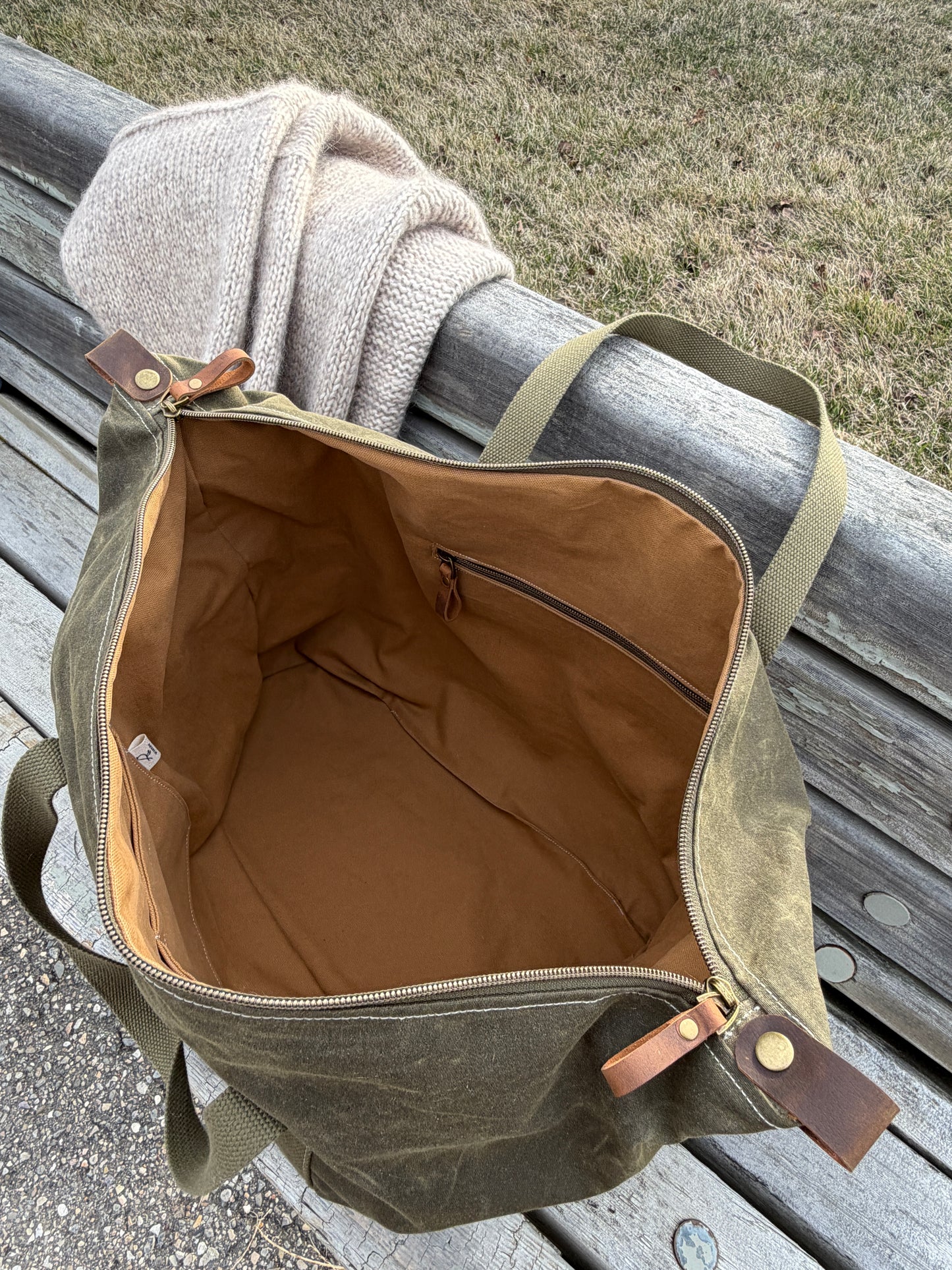Weekender waxed canvas bag in olive green. Shown with top open, exposing cinnamon colored canvas lining and inner zippered pocket. 