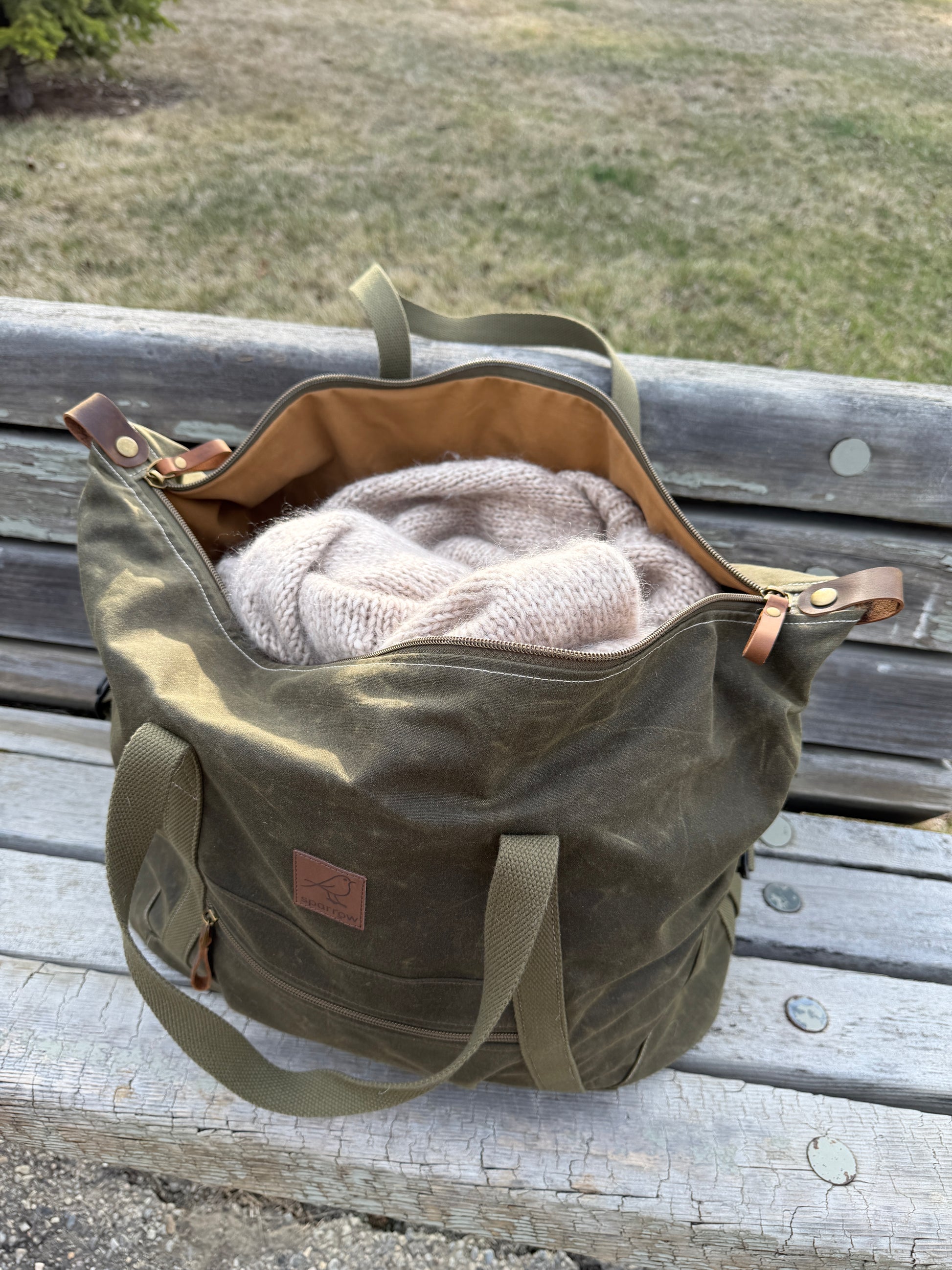 Weekender waxed canvas bag in olive green handmade in Canada by Sparrow Handmade. Shown open with knitted sweater visible inside