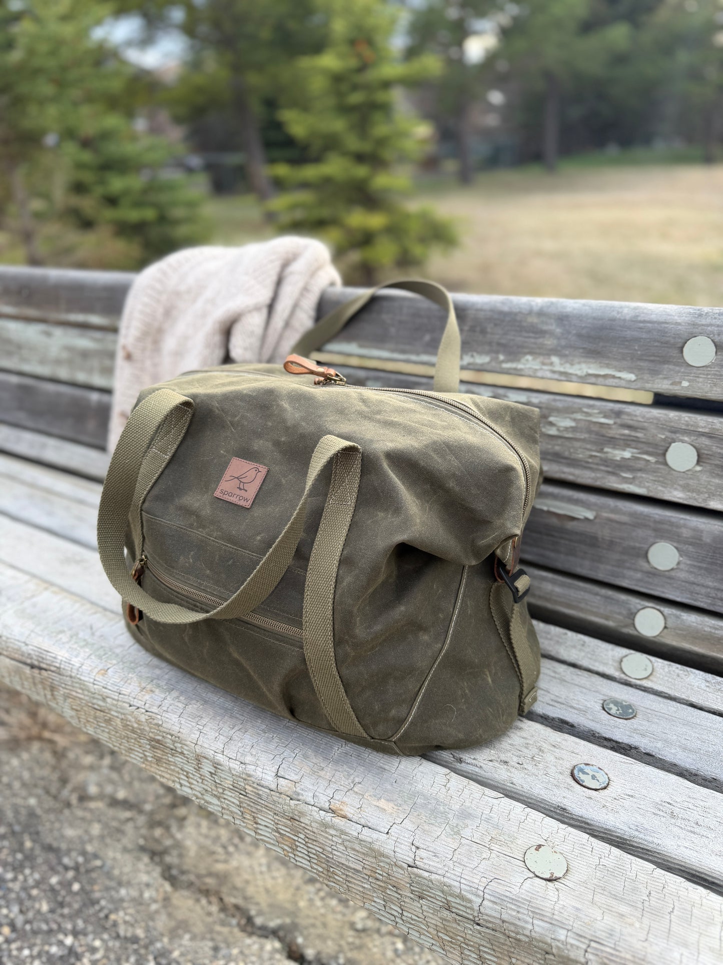 Weekender waxed canvas bag in olive green handmade in Canada by Sparrow Handmade. Sweater is on the bench. 