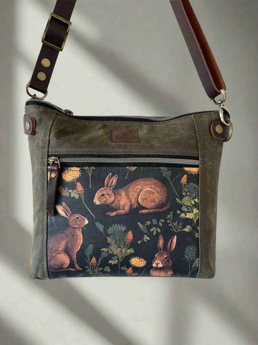 Cambridge crossbody bag in olive waxed canvas and medieval rabbit front pocket accent print, with zippered front pocket and top closure. Handcrafted in Canada by Sparrow Handmade. 