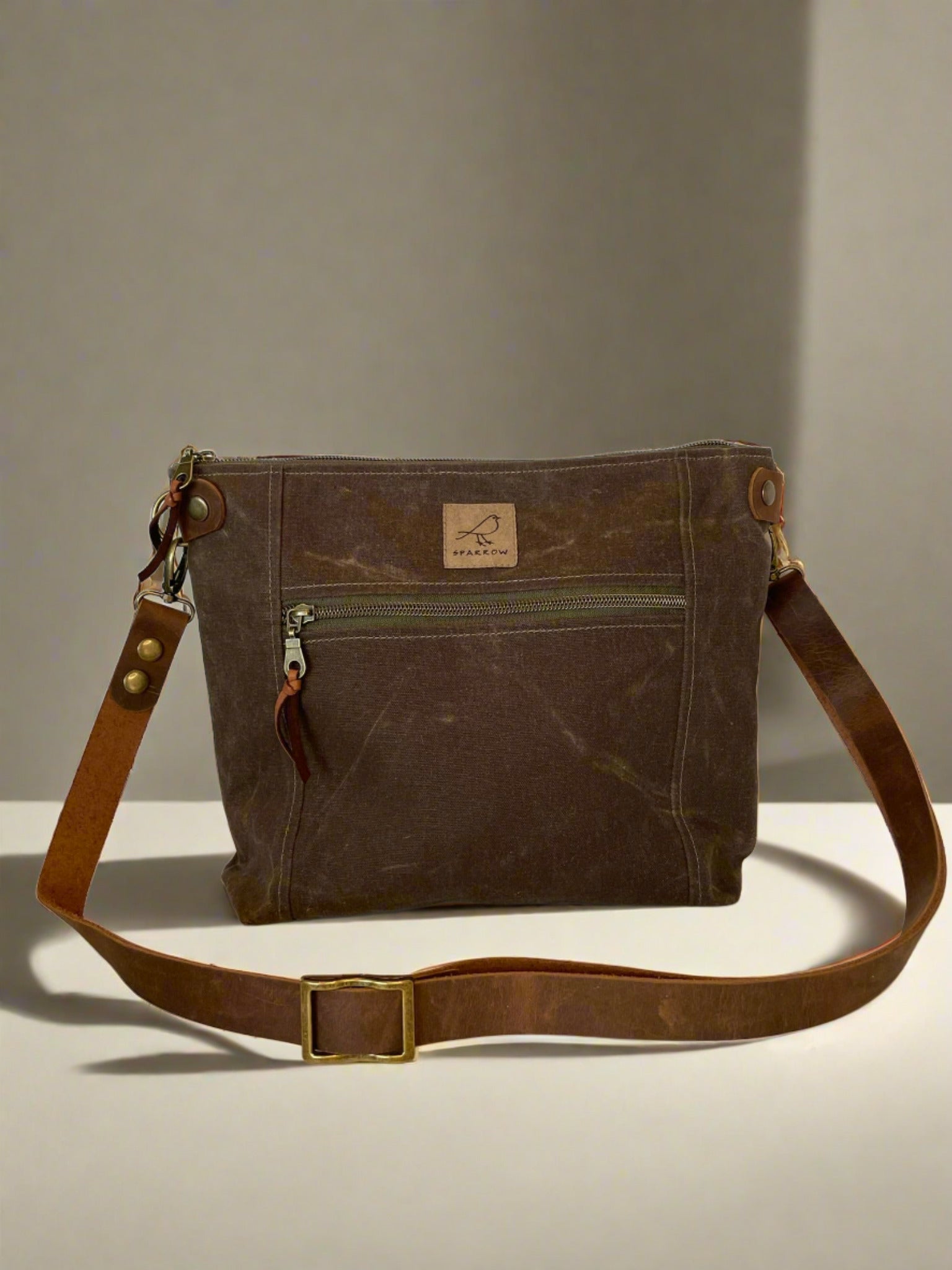 Cambridge crossbody bag in brown waxed canvas with zippered front pocket and top closure. Adjustable leather strap. Handcrafted in Canada by Sparrow Handmade. Ochre label. 